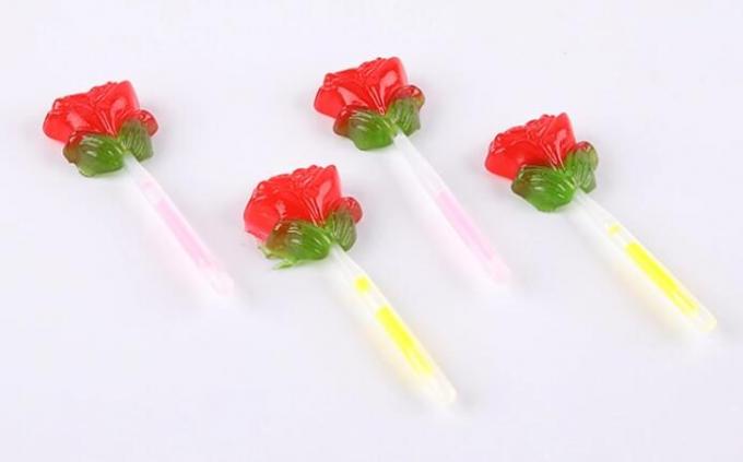 A fluorescência ilumina acima o pirulito da forma da flor de Rosa dos doces com vara da iluminação